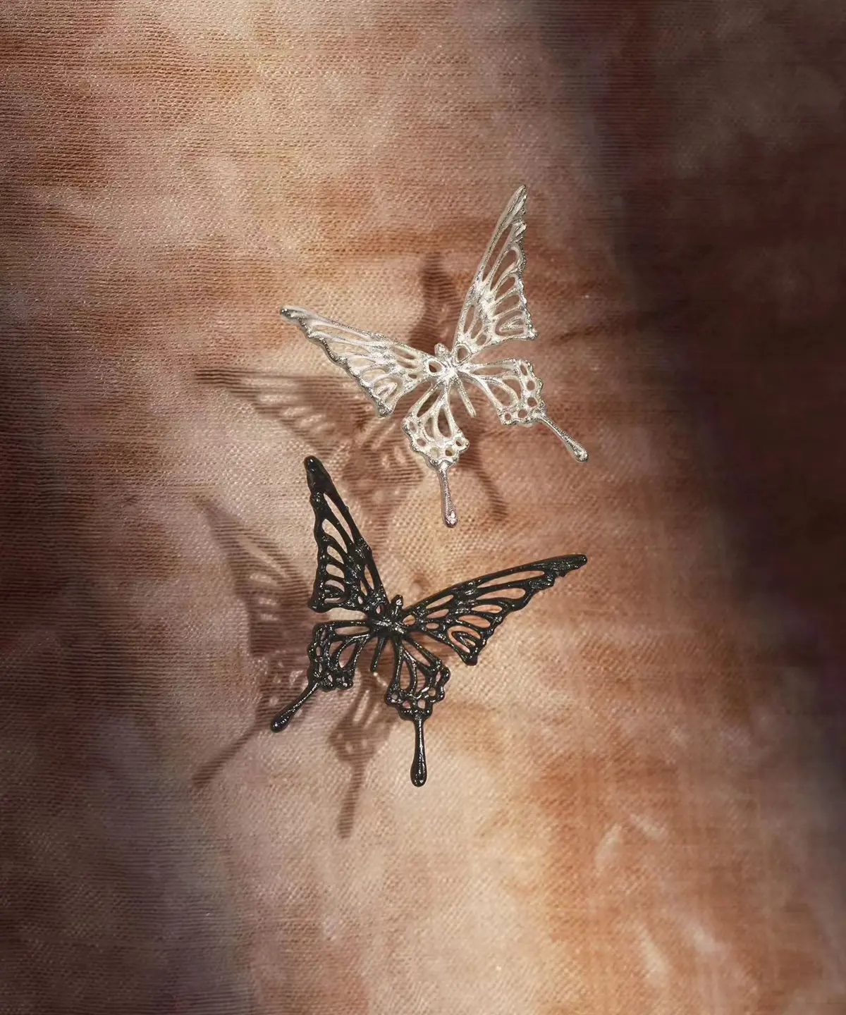The image features two pairs of Dream Butterfly Earrings & Ear Cuffs, one in silver and the other in black, elegantly displayed against a textured brown background. These butterfly earrings are designed to be worn without piercings, offering a delicate yet bold aesthetic.