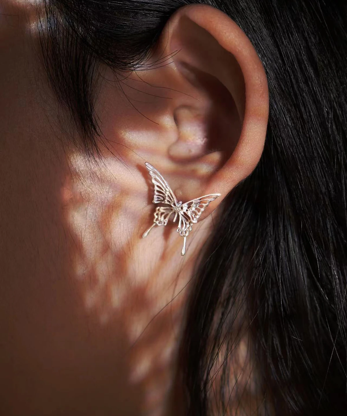 This image captures a detailed close-up of Dream Butterfly Stud Earrings, delicately positioned on the ear. The jewelry showcases an elegant butterfly motif, intricately crafted to highlight its artistic finesse. The soft lighting in the image enhances the delicate details, casting gentle shadows that add dimension to the butterfly earrings. Perfect for those seeking ethereal, nature-inspired jewelry with a seamless and adjustable fit.