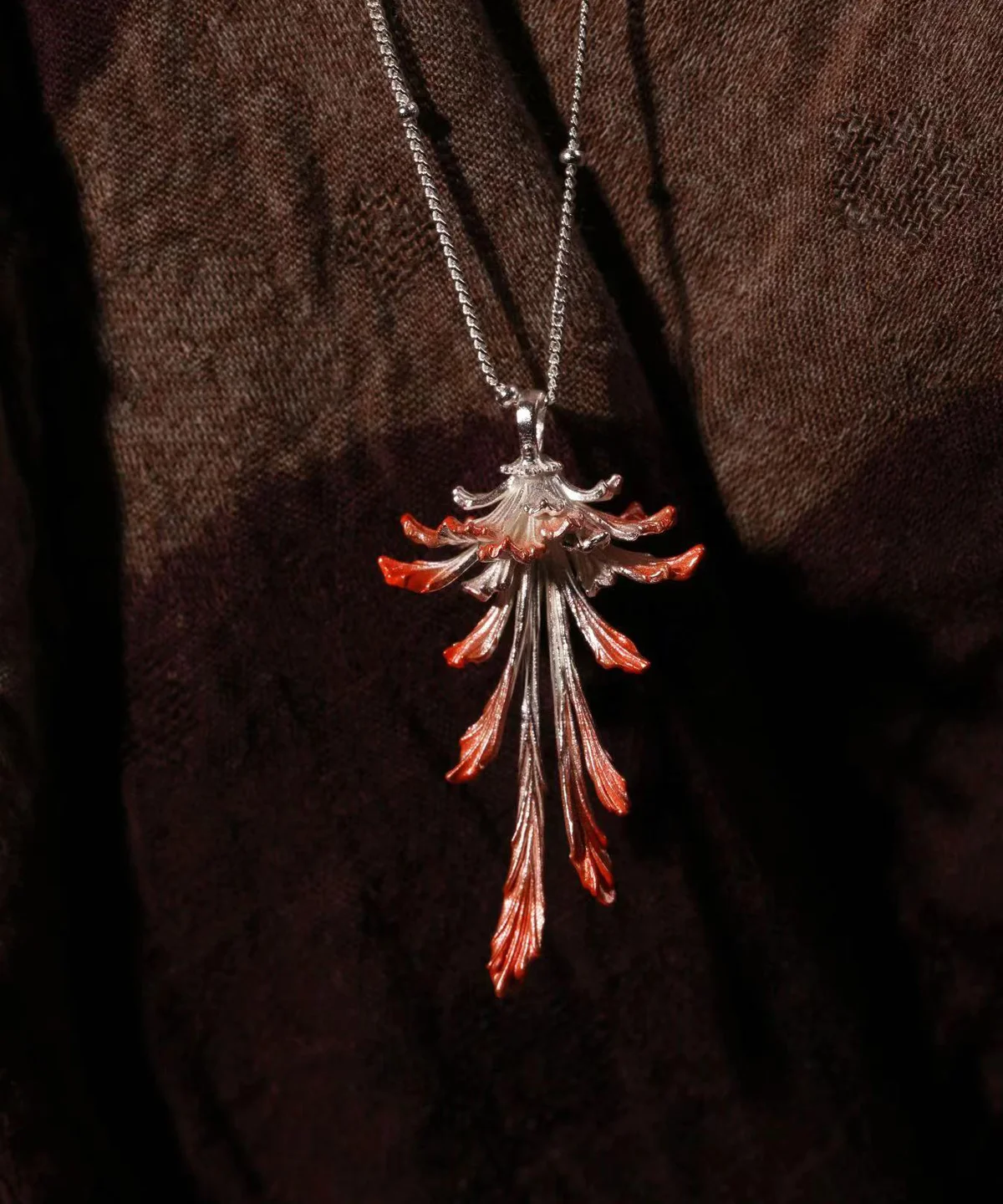 Drooping Blossom | 925 Sterling Silver Long Necklace features a meticulously crafted floral pendant in sterling silver, with elongated petals accented by subtle copper hues. Hanging from a delicate long chain, the pendant is showcased against a dark textured backdrop that highlights its detailed artistry. This elegant piece seamlessly blends modern sophistication with timeless charm, making it perfect for both casual and formal occasions.