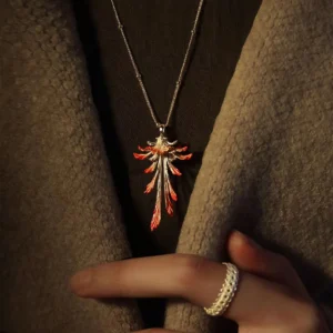 Drooping Blossom | 925 Sterling Silver Long Necklace showcases a delicately crafted blossom pendant with intricate silver detailing and subtle red accents, suspended from a fine chain. The product is set against a textured coat backdrop with a hand adorned by a woven silver ring, emphasizing sophistication. This refined accessory, ideal for both casual and formal wear, highlights exceptional craftsmanship and timeless style.