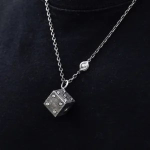 This handcrafted sterling silver necklace features a dice-inspired cube pendant with a rough texture and subtle eye-shaped engravings. The twisted metallic chain, enhanced by a delicate eye motif, complements the pendant's artistic design. Set against a dark backdrop, the piece highlights intricate craftsmanship and a unique, symbolic aesthetic.