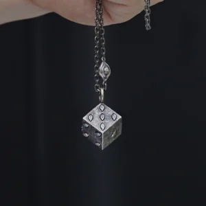 A close-up view of a handcrafted sterling silver necklace featuring a unique six-sided dice pendant. The metallic dice is elegantly adorned with intricate engravings and gem-like accents that add a refined touch. A medium-thickness chain complements the pendant, and the dark background highlights its lustrous texture. This Prison Realm Dice Necklace showcases a striking blend of bold design and skilled, artisanal craftsmanship.
