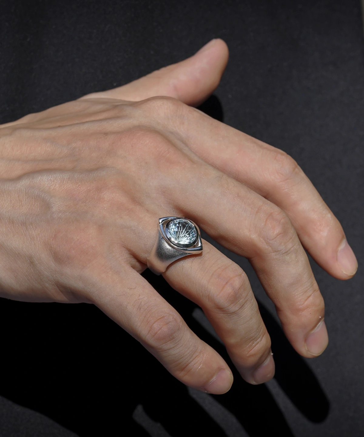 A close-up of a hand adorned with the Six Eyes Ring in Sterling Silver, featuring a striking natural topaz. The intricate craftsmanship and luminous gemstone contrast against a dark background, enhancing its brilliance.