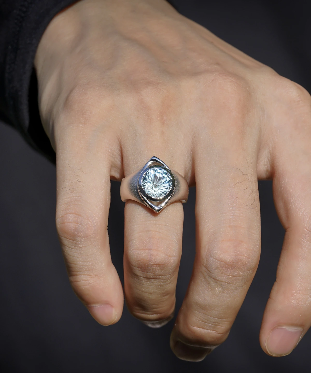 A close-up of a hand adorned with the Six Eyes Ring in Sterling Silver, featuring a striking natural topaz. The intricate craftsmanship and luminous gemstone contrast against a dark background, enhancing its brilliance.