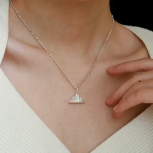 A person wearing the Snow Mountain Necklace with a 999 Pure Silver Pendant, featuring a triangular, snow-capped mountain design. The fine silver chain complements the pendant’s elegant craftsmanship. The person is dressed in a light-colored, textured top, providing a subtle background to highlight the necklace’s details.