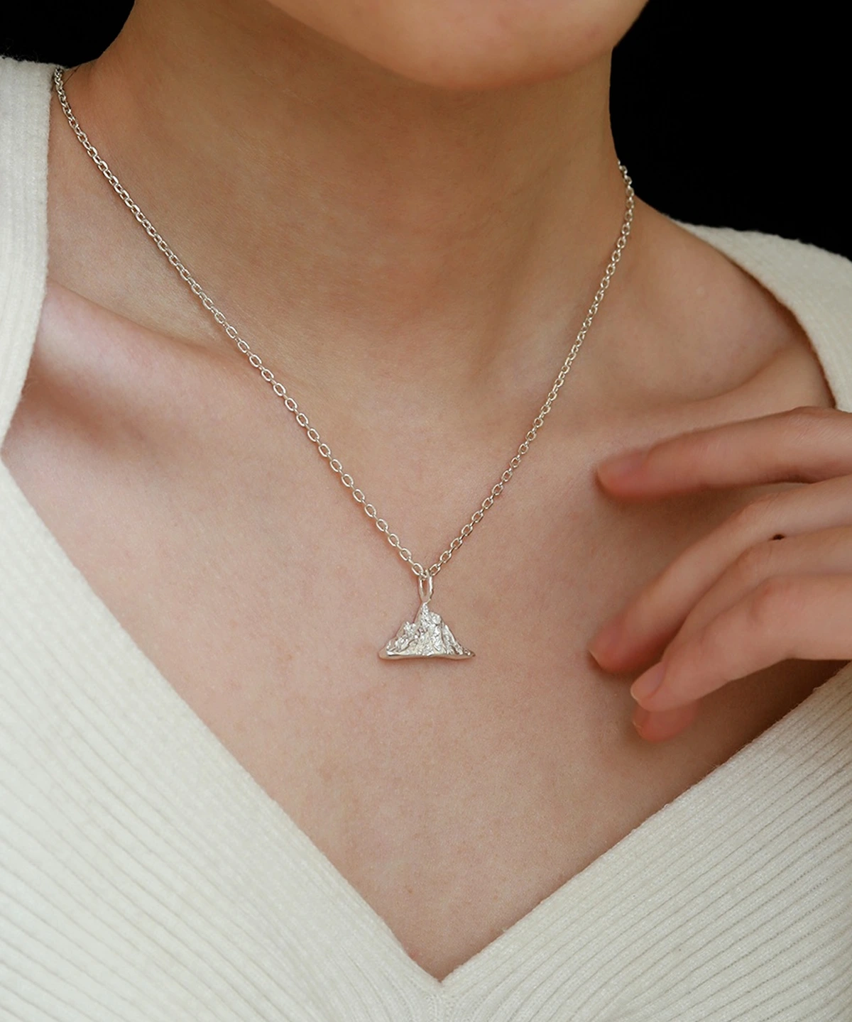 A person wearing the Snow Mountain Necklace with a 999 Pure Silver Pendant, featuring a triangular, snow-capped mountain design. The fine silver chain complements the pendant’s elegant craftsmanship. The person is dressed in a light-colored, textured top, providing a subtle background to highlight the necklace’s details.