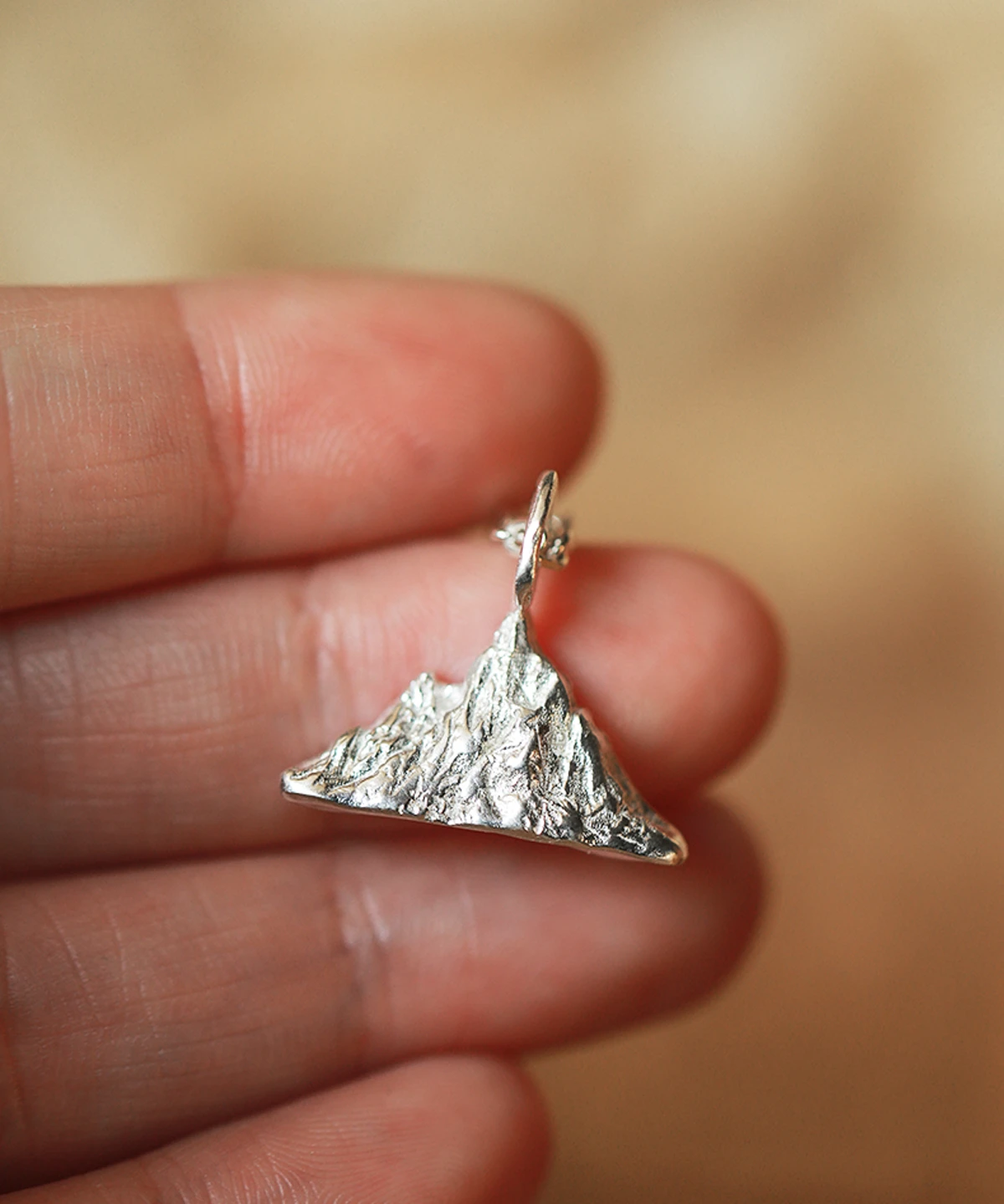 A close-up of a hand holding the Snow Mountain Necklace – 999 Pure Silver Pendant, which features a detailed mountain range design. The peaks and valleys are finely crafted, showcasing the purity and brilliance of 999 silver.