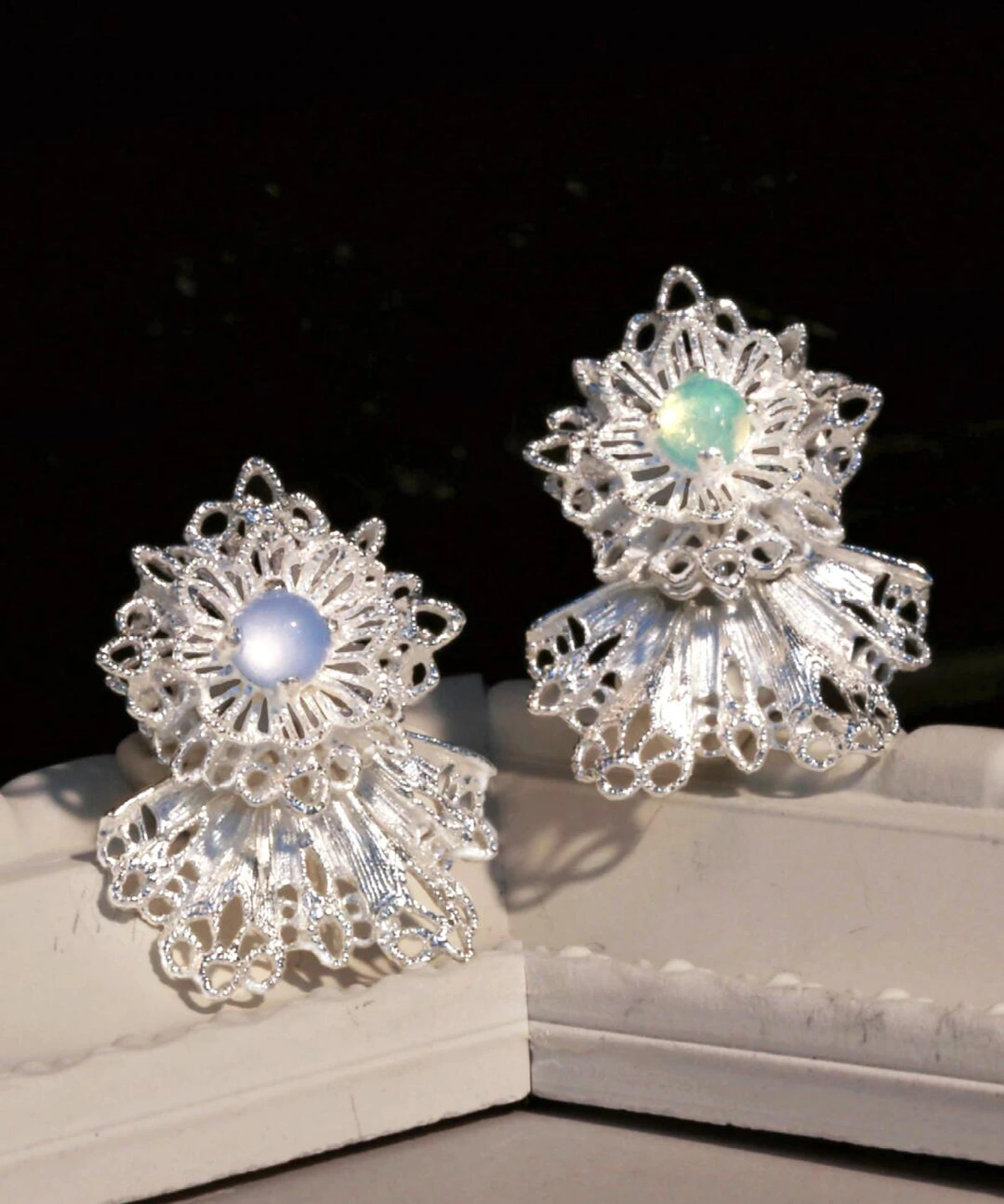 These Snowflake Earrings embody delicate artistry and winter-inspired elegance. Crafted from 925 sterling silver, each earring features an intricate lace-like snowflake design, capturing the beauty of frost-kissed patterns. At the heart of each piece sits a shimmering gemstone—one in a serene blue hue and the other in a soft green—adding a subtle yet mesmerizing touch of color. The silver framework reflects light gracefully, enhancing its refined allure. Displayed against a contrasting dark background, these earrings exude sophistication, making them a perfect blend of seasonal charm and timeless craftsmanship.