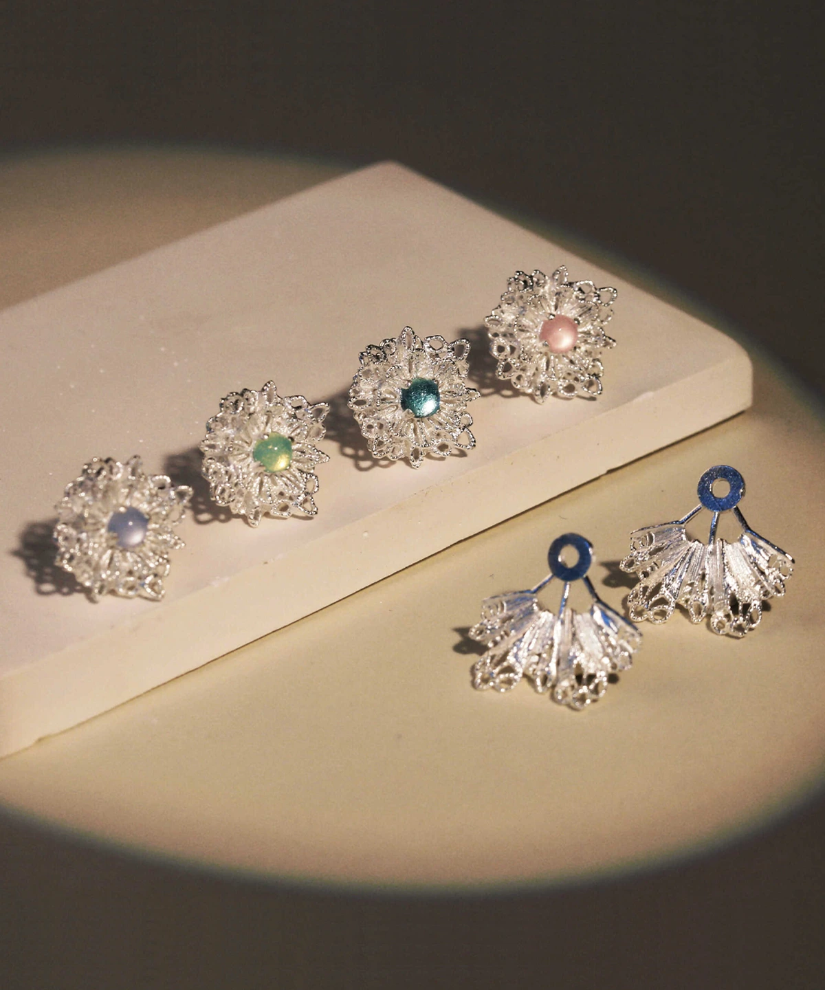 Snowflake Earrings displayed on a neutral-toned surface. These 925 Sterling Silver Lace Stud Earrings feature intricate snowflake-inspired lace patterns, paired with matching fan-shaped drop elements adorned with vibrant gemstone accents in shades of blue, green, and pink.