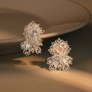 The image features a pair of Snowflake Earrings crafted from 925 sterling silver lace. Each earring showcases an intricate snowflake design with delicate silver filigree, centered around a gemstone—one in soft pink and the other in light purple.