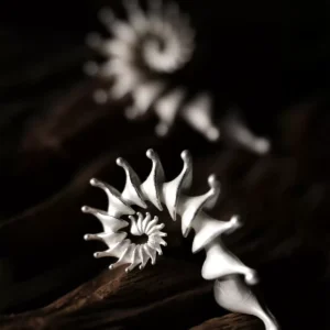 A close-up image of two Spiral Earrings made from S925 sterling silver, designed as Designer Ear Cuffs. The earrings feature an elegant, flowing spiral structure with smooth curves and pointed tips, presented against a rustic wooden background.