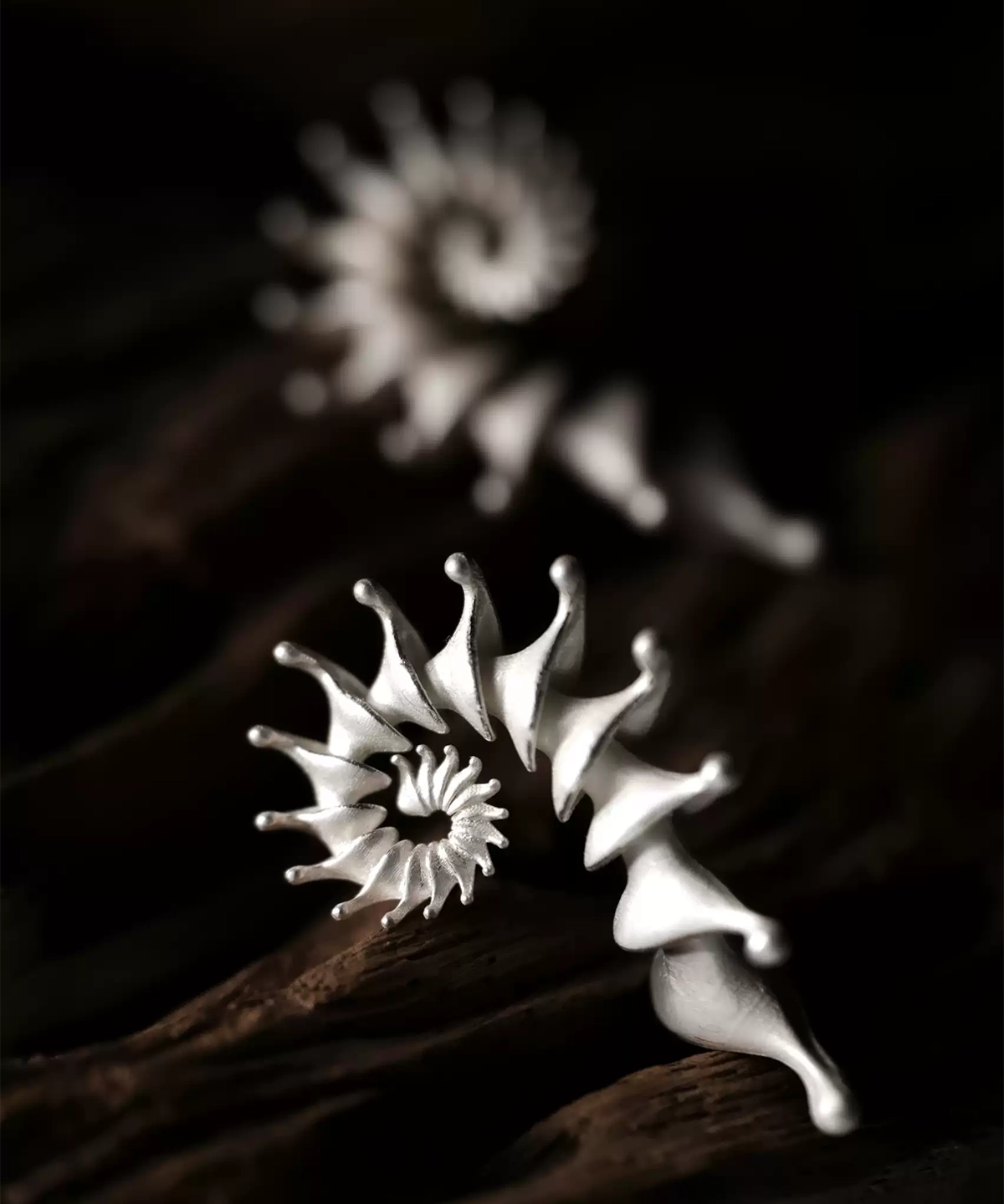 A close-up image of two Spiral Earrings made from S925 sterling silver, designed as Designer Ear Cuffs. The earrings feature an elegant, flowing spiral structure with smooth curves and pointed tips, presented against a rustic wooden background.