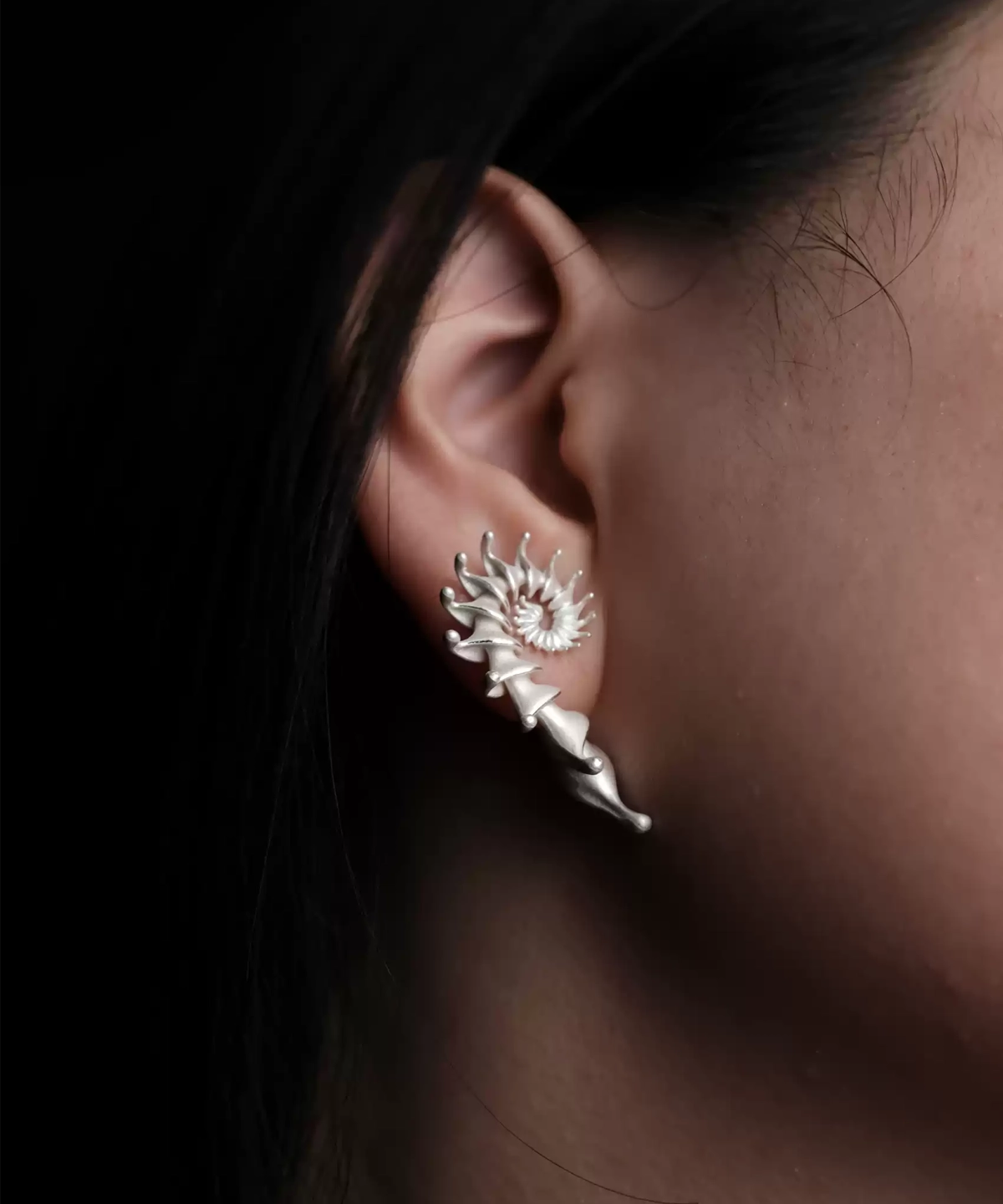 Close-up view of a left ear adorned with the Spiral Earrings | S925 Sterling Silver Designer Ear Stud. This silver earring features a striking spiral design, wrapping along the ear with its refined, pointed tips for a bold and artistic statement.