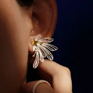A close-up of a woman's ear showcases the Star Trail 925 Sterling Silver Star Stud Earrings, featuring delicate silver loops and gold star accents radiating from a central gold star. The design evokes the motion of a shooting star.