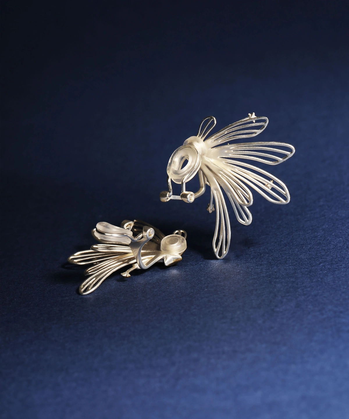 A detailed view of the Star Trail-925 Sterling Silver Star Stud Earrings & Ear Cuffs displayed against a deep blue background, highlighting the intricate starburst design, lightweight wire structure, and secure stud clasp at the back.