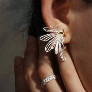 A close-up of a woman wearing the Star Trail 925 Sterling Silver Star Stud Earrings, designed with flowing silver loops and accented by small gold stars radiating from a central golden star, creating an elegant, celestial-inspired look.