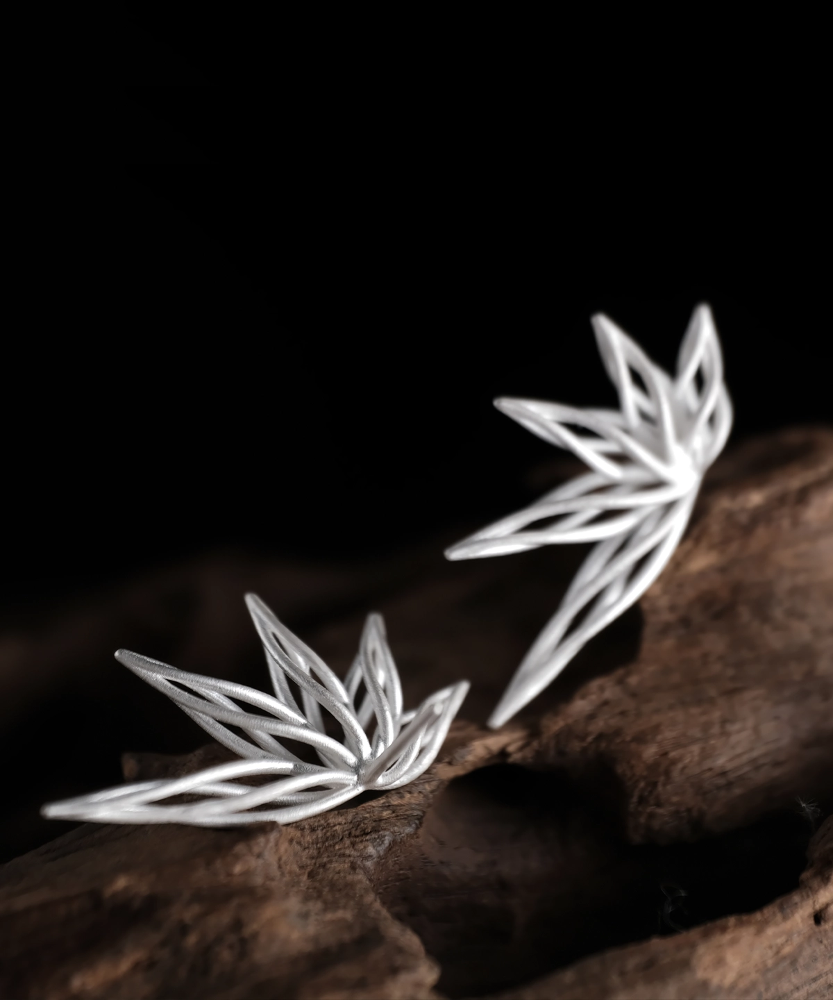 Organic sterling silver statement earrings with a fluid petal-inspired design, showcased on a wooden surface.