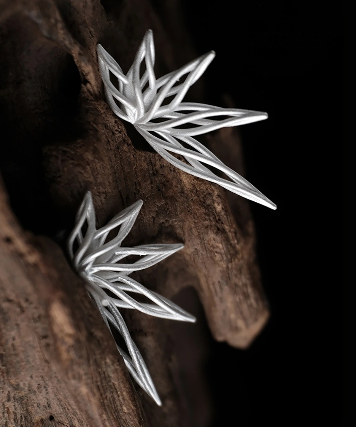 Organic sterling silver statement earrings featuring a flowing petal-inspired design, elegantly displayed on a rustic wooden surface.