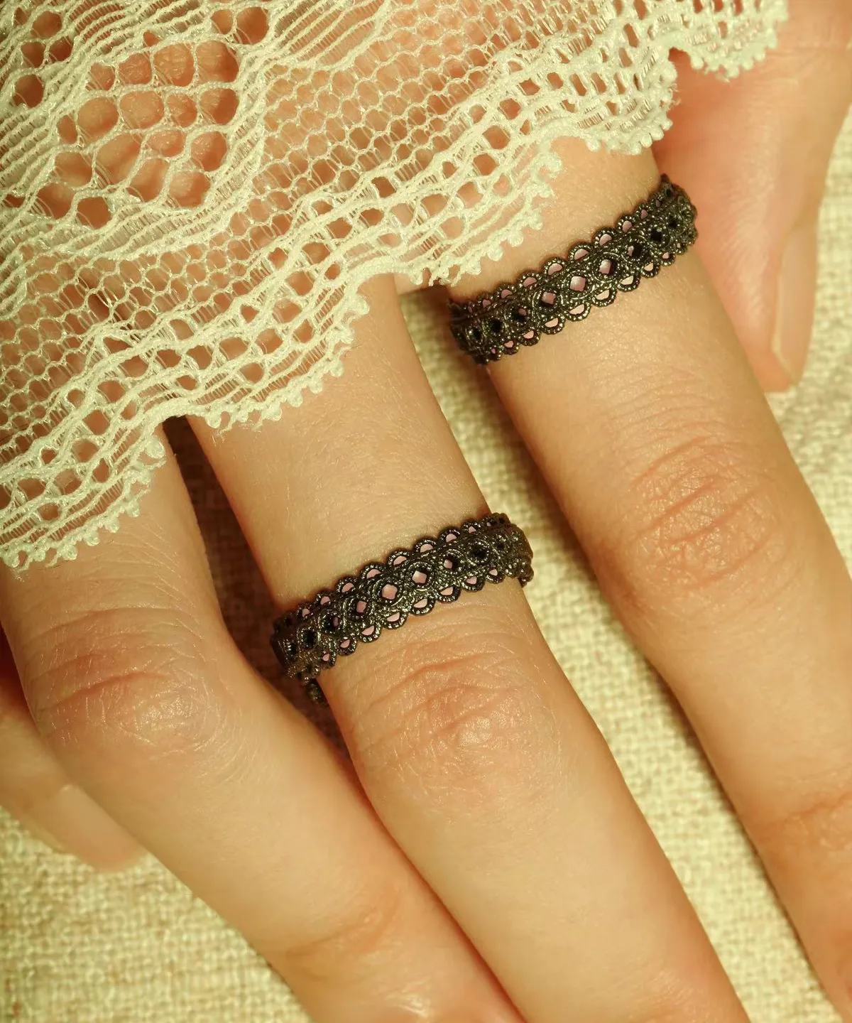 A close-up of two fingers wearing intricately designed Lace Rings crafted from S925 sterling silver. These adjustable rings feature a detailed vintage lace pattern, creating an elegant and artistic aesthetic. The fingers are partially draped in delicate white lace fabric, enhancing the refined look.