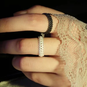 A close-up image of a hand adorned with two lace rings, one black and one silver, showcasing intricate lace-like designs. The hand is partially covered by a delicate lace fabric, highlighting the vintage and handmade craftsmanship of the rings. The rings are adjustable and made of S925 sterling silver.
