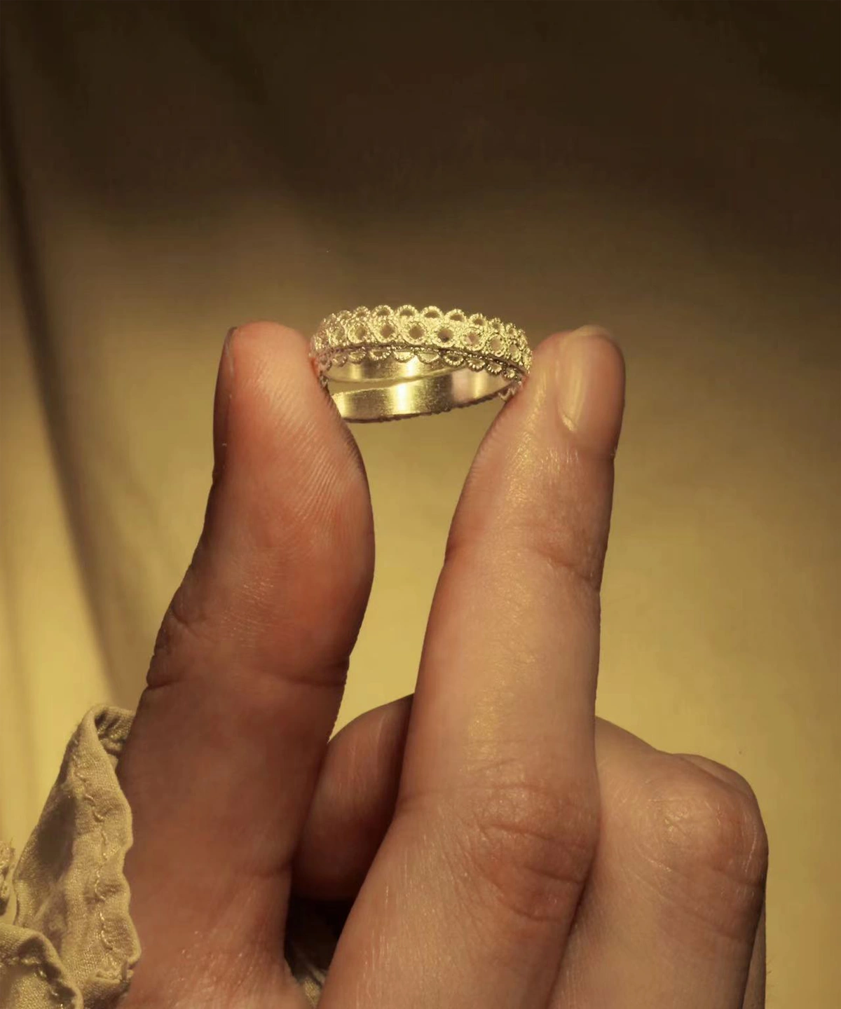 A close-up image of a hand holding a Lace Ring made of S925 Sterling Silver. The ring features intricate lace-like patterns and is adjustable. The background is a warm, golden hue, highlighting the elegance of this handmade art jewelry piece.