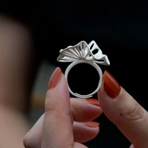 A close-up of a hand showcasing a 925 silver adjustable leaf ring with delicate cutouts and a freshwater pearl accent. The ring's intricate leaf design highlights fine craftsmanship, while the dark background enhances its elegance and detail.
