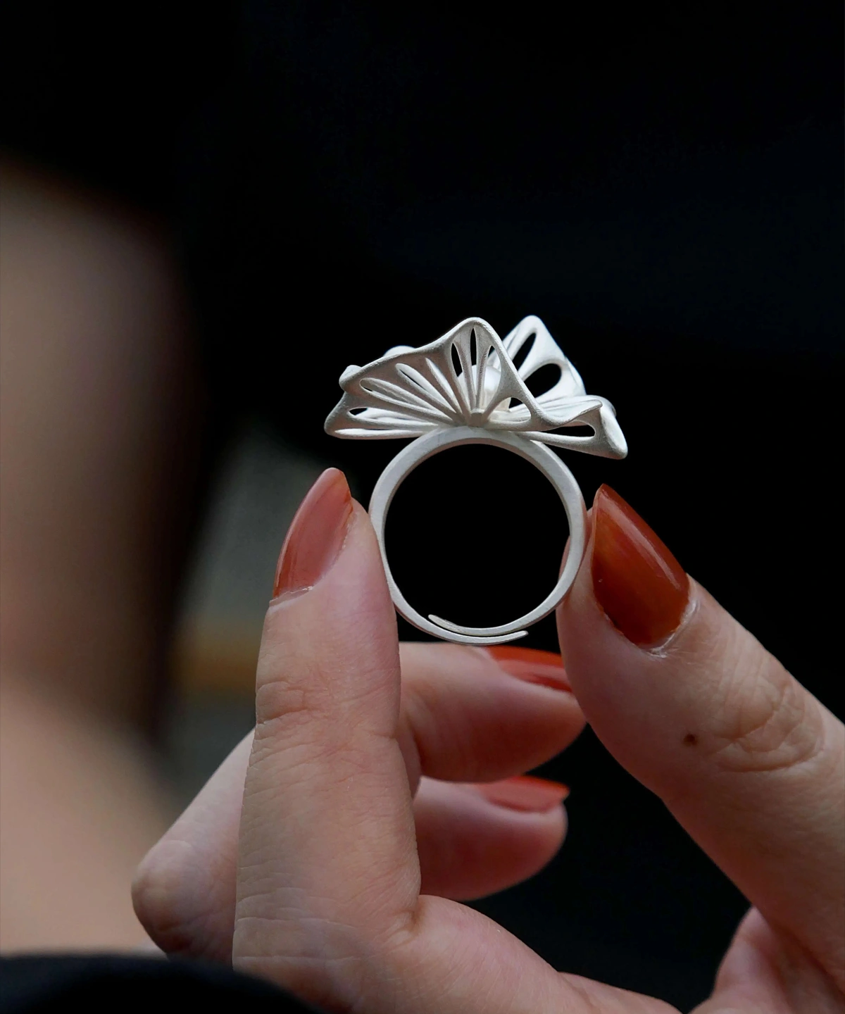 A close-up of a hand showcasing a 925 silver adjustable leaf ring with delicate cutouts and a freshwater pearl accent. The ring's intricate leaf design highlights fine craftsmanship, while the dark background enhances its elegance and detail.