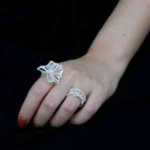 A close-up of a hand wearing a 925 silver adjustable leaf ring with a freshwater pearl on the index finger. The ring features an intricate leaf design, symbolizing elegance and nature-inspired beauty. Another ring with a similar design is worn on the middle finger. The black background enhances the visual appeal.