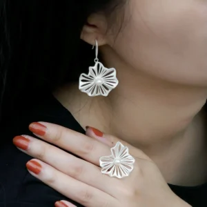 A woman's hand elegantly showcases a 925 silver adjustable leaf ring with a freshwater pearl, accompanied by matching leaf-shaped earrings. The delicate design of the ring features intricate silver detailing resembling leaves, embracing a luminous central pearl. The jewelry complements her reddish-brown nail polish, creating a sophisticated and stylish look.