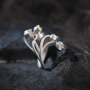A close-up image of a Lily of the Valley Ring made from S925 sterling silver. The ring features an open design with delicate, handcrafted lily of the valley flowers, elegantly positioned on a dark, textured background.