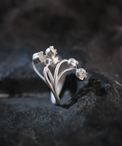 A close-up image of a Lily of the Valley Ring made from S925 sterling silver. The ring features an open design with delicate, handcrafted lily of the valley flowers, elegantly positioned on a dark, textured background.