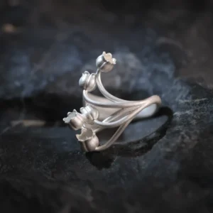 A close-up image of a Lily of the Valley Ring made from S925 sterling silver. The ring features an open design with delicate, handcrafted lily of the valley flowers, elegantly positioned on a dark, textured background.