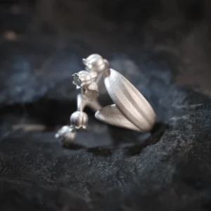 Close-up of a Lily of the Valley Ring crafted from S925 sterling silver. One side features delicately sculpted lily of the valley flowers, while the other side showcases intricate leaf detailing. The silver open ring design is adjustable for a custom fit.