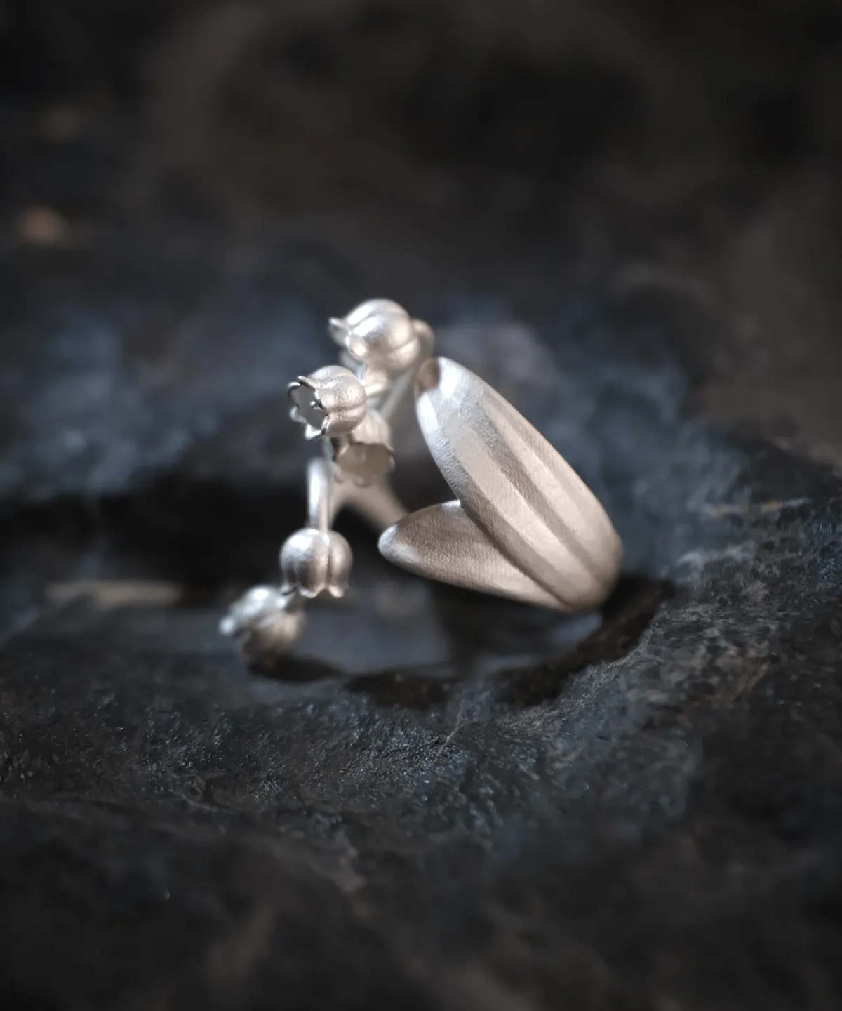 Close-up of a Lily of the Valley Ring crafted from S925 sterling silver. One side features delicately sculpted lily of the valley flowers, while the other side showcases intricate leaf detailing. The silver open ring design is adjustable for a custom fit.