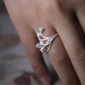 A close-up image of a hand wearing the Lily of the Valley Ring, crafted in S925 sterling silver. The silver open ring features delicate, bell-shaped flowers gracefully extending from the adjustable band.