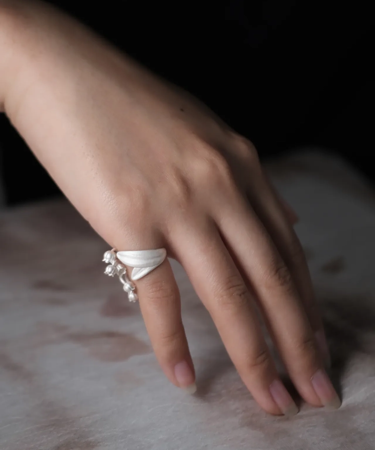 A close-up of a hand wearing the Lily of the Valley Ring, an S925 sterling silver open ring adorned with delicate lily of the valley flowers. The ring is adjustable and handcrafted for an elegant finish.