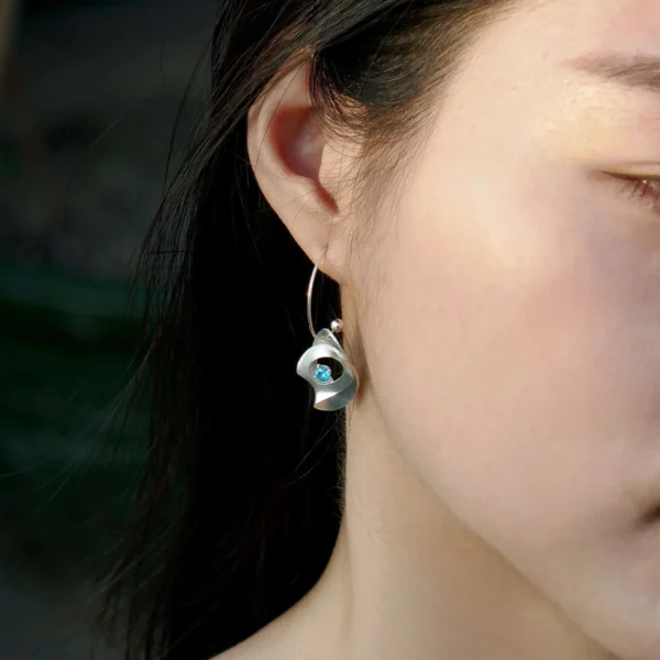Nebula-S925 Silver Sculptural Drop Earrings 01 Close-up of a model wearing Lazesoul’s Nebula S925 Sculptural Silver Drop Earrings, handcrafted with artistic curves and adorned with a blue sapphire gemstone, capturing elegance and modern design.