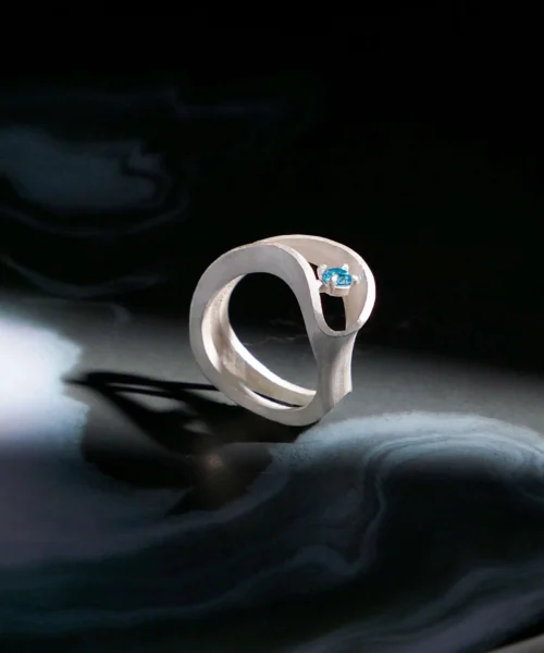 A detailed, close-up image of the Nebula S925 Sterling Silver Sculptural Ring showcasing an intricately hand-sculpted design with swirling, nebula-inspired textures and a brilliant blue sapphire accent—an exquisite example of a Silver Sculptural Ring by Lazesoul Handmade Art Jewelry.