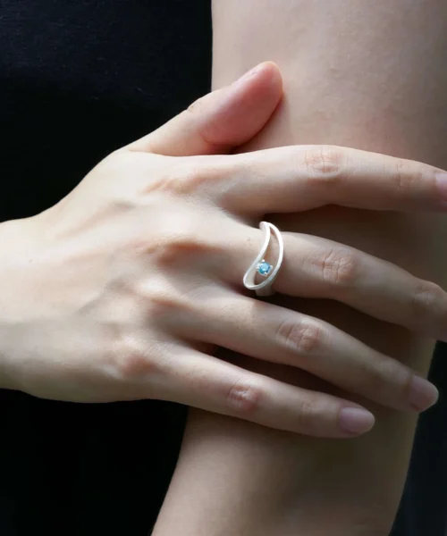 Close-up view of a woman's hand adorned with the Nebula S925 Sterling Silver Sculptural Ring by Lazesoul, showcasing its elegant, fluid design and striking blue sapphire centerpiece – a unique piece of handmade silver art jewelry that blends craftsmanship with celestial inspiration.