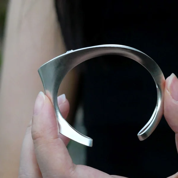 Nebula-Sculptural S925 Sterling Silver Open Bangle 02 Hand holding the Nebula Sculptural S925 Sterling Silver Open Bangle by Lazesoul, featuring a curved modern design with a polished finish and blue sapphire accent, handmade silver open bangle in focus.
