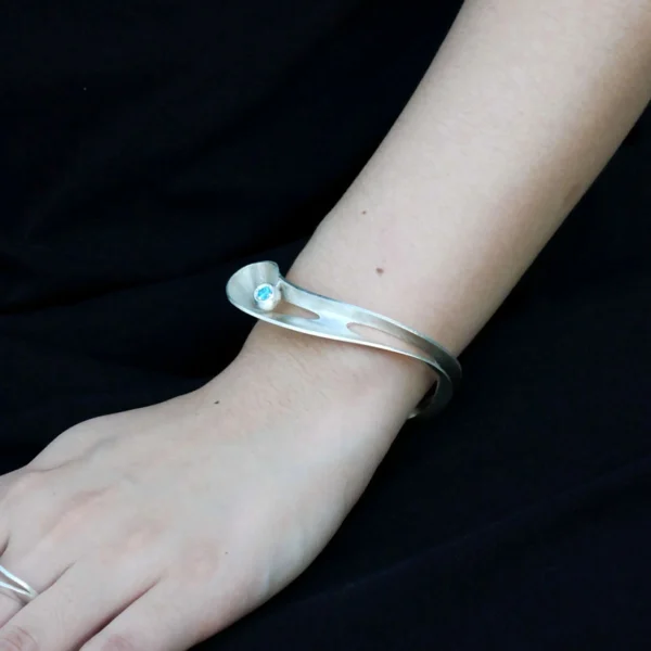 Nebula-Sculptural S925 Sterling Silver Open Bangle 04 A model’s wrist adorned with the Lazesoul Nebula Sculptural S925 Sterling Silver Open Bangle, featuring an organic, artistic silver twist and a deep blue sapphire detail. Handmade art jewelry designed for elegance and style.