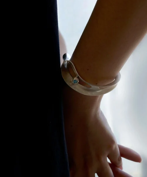 Close-up of a wrist wearing the Nebula Sculptural S925 Sterling Silver Open Bangle with blue sapphire, showcasing Lazesoul’s handmade art jewelry design in soft lighting.