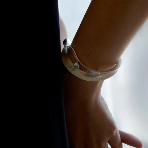 Nebula-Sculptural S925 Sterling Silver Open Bangle 06 Close-up of a wrist wearing the Nebula Sculptural S925 Sterling Silver Open Bangle with blue sapphire, showcasing Lazesoul’s handmade art jewelry design in soft lighting.