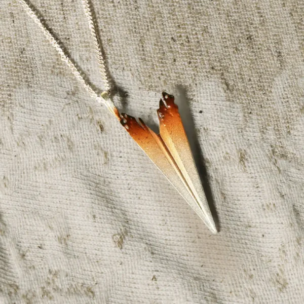 A handmade S925 sterling silver necklace featuring a paper airplane pendant with a gradient design from silver to brown, displayed on a textured fabric background.