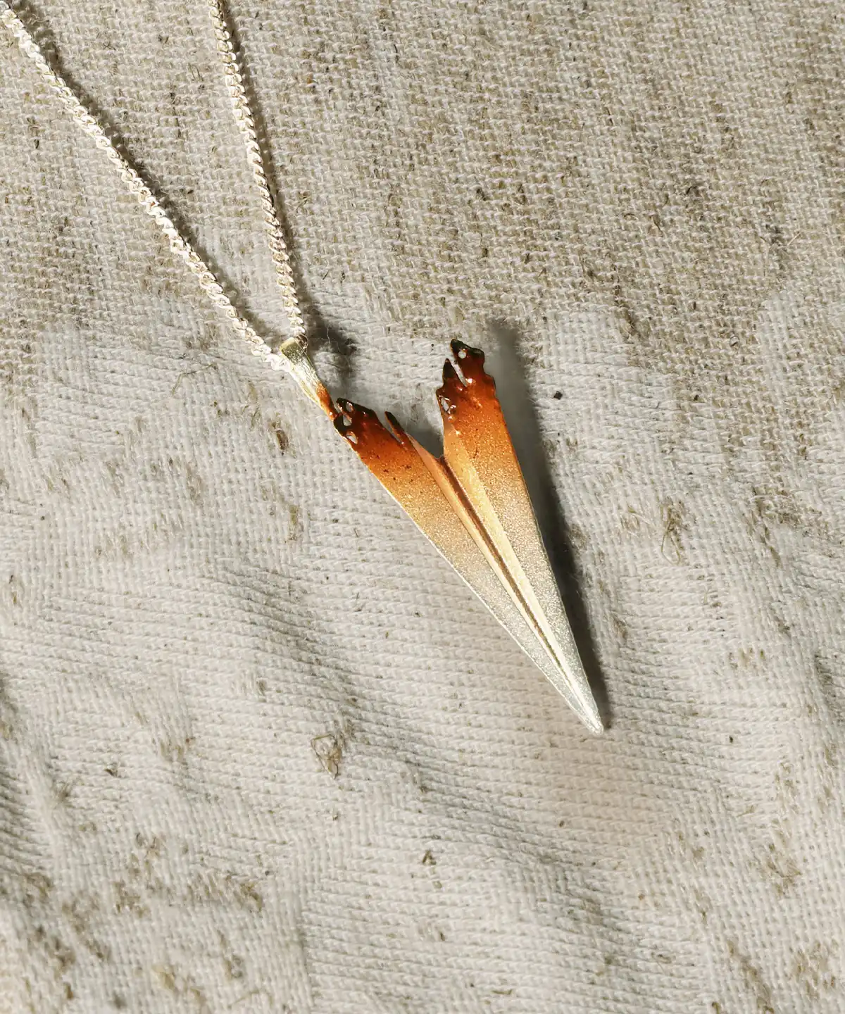 A handmade S925 sterling silver necklace featuring a paper airplane pendant with a gradient design from silver to brown, displayed on a textured fabric background.