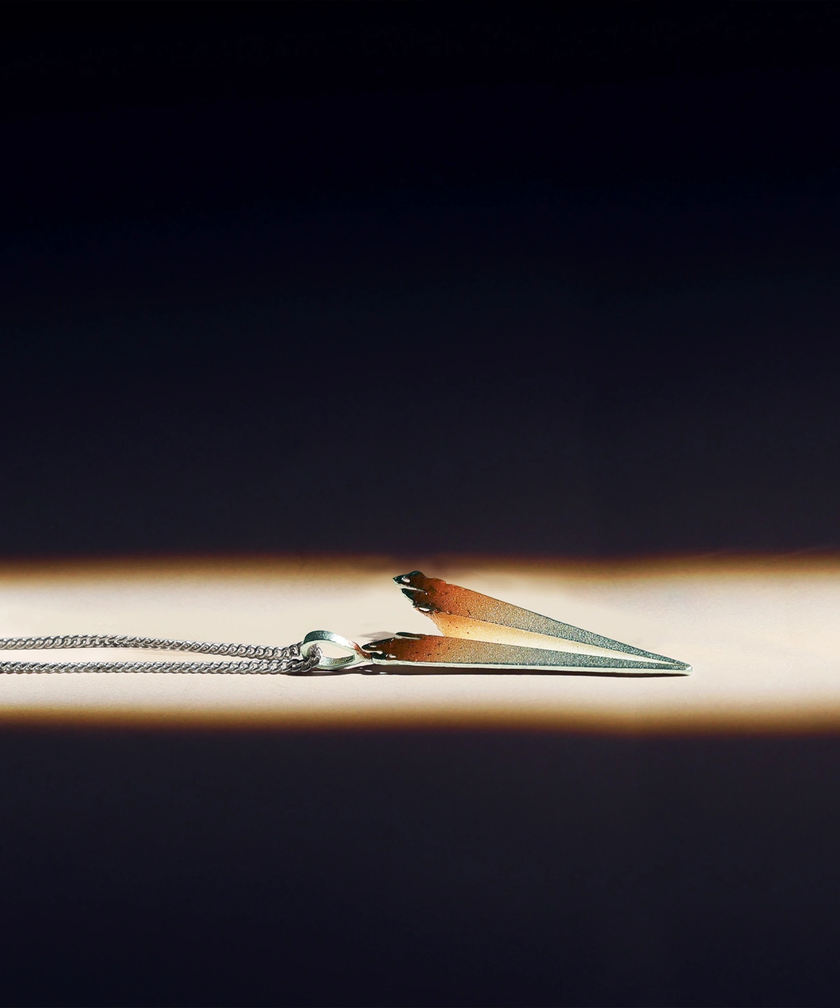A close-up image of a handmade S925 sterling silver paper airplane necklace. The necklace features a delicate chain and a pendant shaped like a paper airplane, with a gradient color effect transitioning from silver to a warm brown hue.