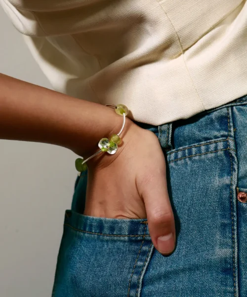 A stylish woman's hand rests casually in a pocket, adorned with the Lazesoul Prelude Summer Peridot Bracelet—crafted from S925 sterling silver with natural prehnite and peridot beads; handmade elegance captured in detail.