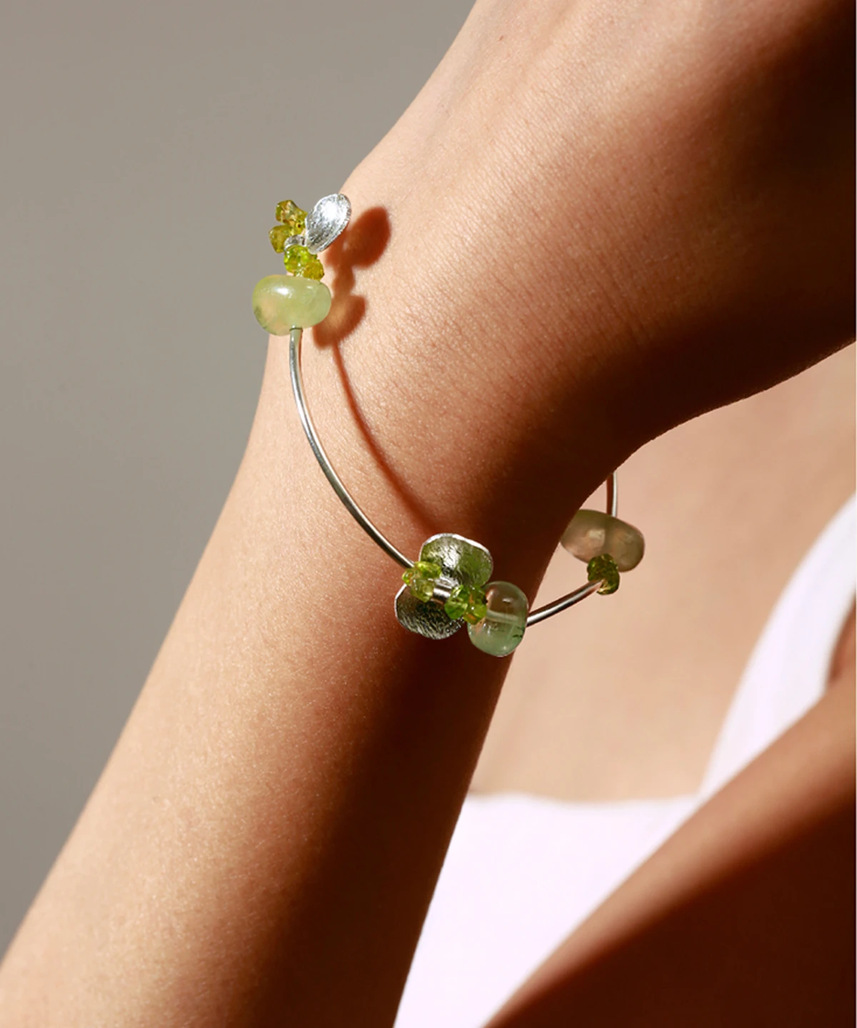 Elegant close-up of a wrist wearing the Prelude Summer Peridot Bracelet, handcrafted in S925 sterling silver with natural green prehnite and peridot stones, highlighting its artisan charm and luminous gemstone details.