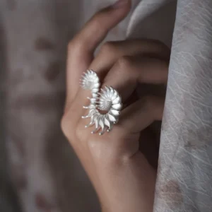 A close-up image of a hand adorned with a Spiral Ring crafted from S925 sterling silver. The ring’s sculptural design elegantly wraps around the finger, creating a fluid, artistic silhouette. Its polished silver surface catches the light, accentuating the organic spiral form. The softly blurred background enhances the ring's presence, highlighting its contemporary yet timeless appeal as a statement piece in modern jewelry design.