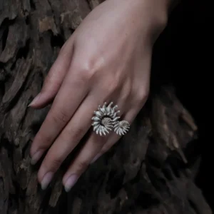 A close-up shot of a hand adorned with a Spiral Ring crafted from S925 sterling silver. The ring features an intertwined, sculptural design, elegantly wrapping around the finger. The hand is placed against a textured wooden backdrop, complementing the organic aesthetic of the jewelry.